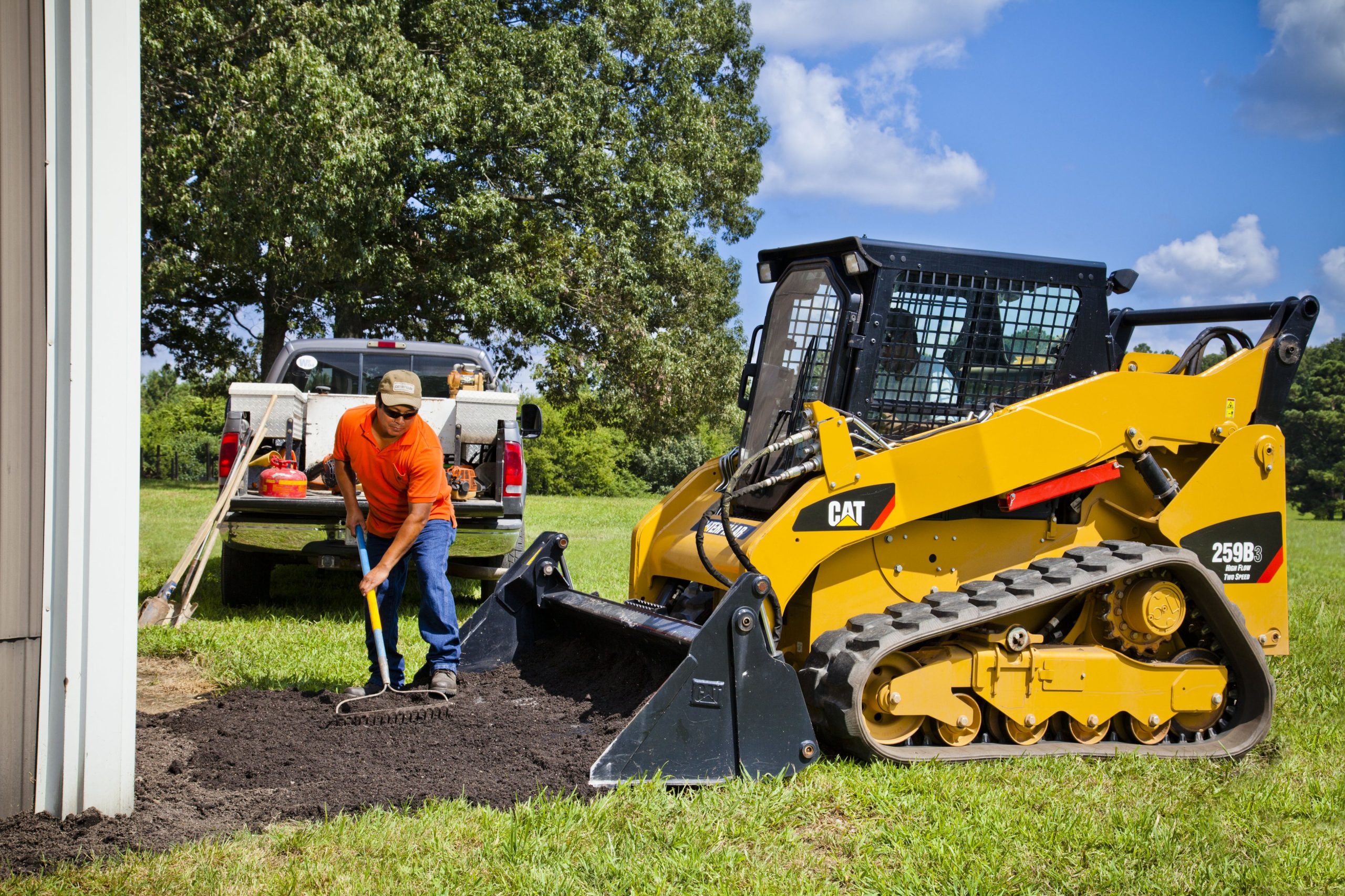 Man raking dirt in front of CAT equipment